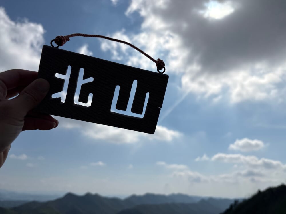 北山の手作り山頂看板を空に掲げた写真